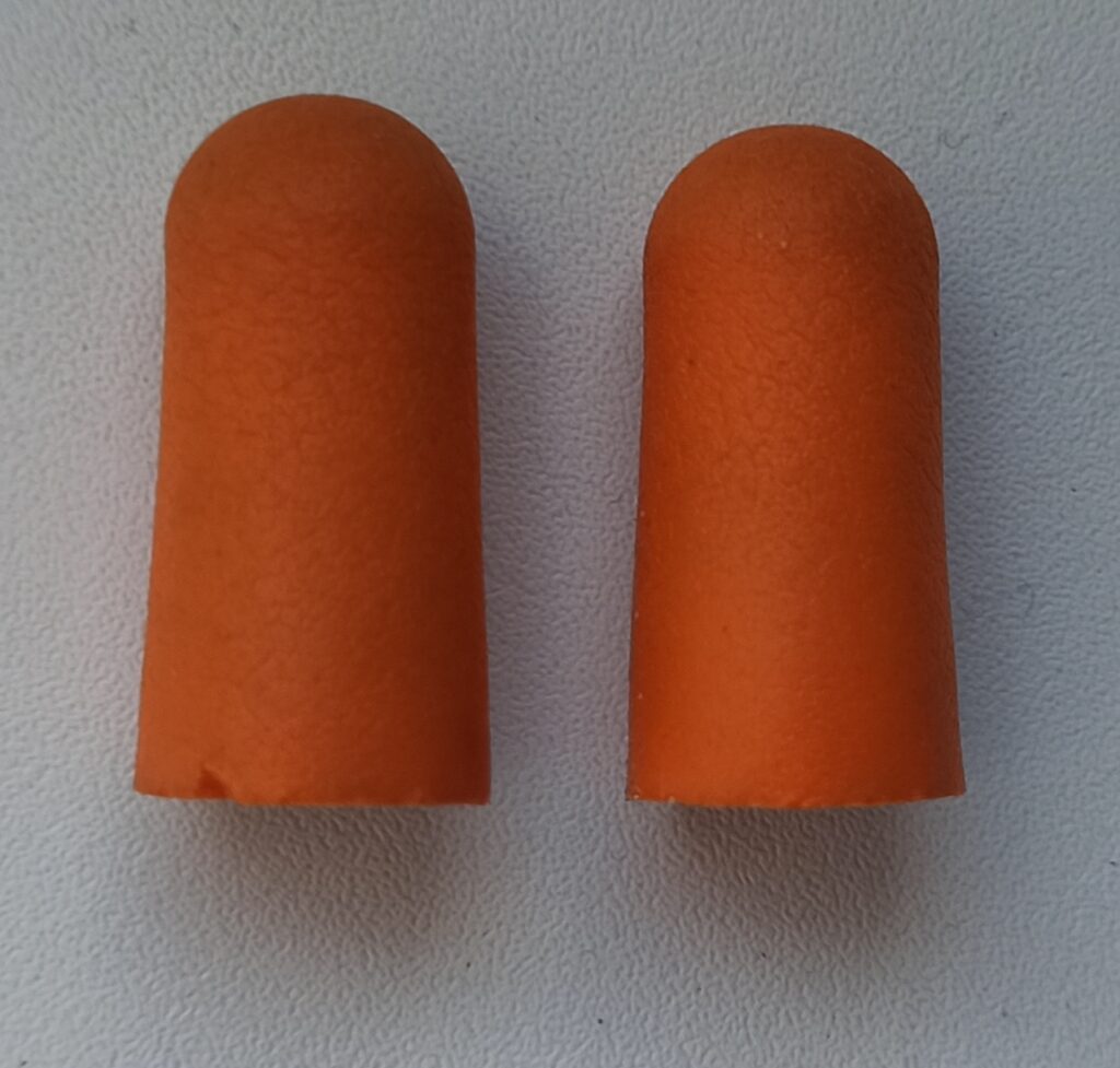 Deux bouchons d'oreilles en mousse pos&eacute;s sur une table claire &agrave; c&ocirc;t&eacute; d'un carnet