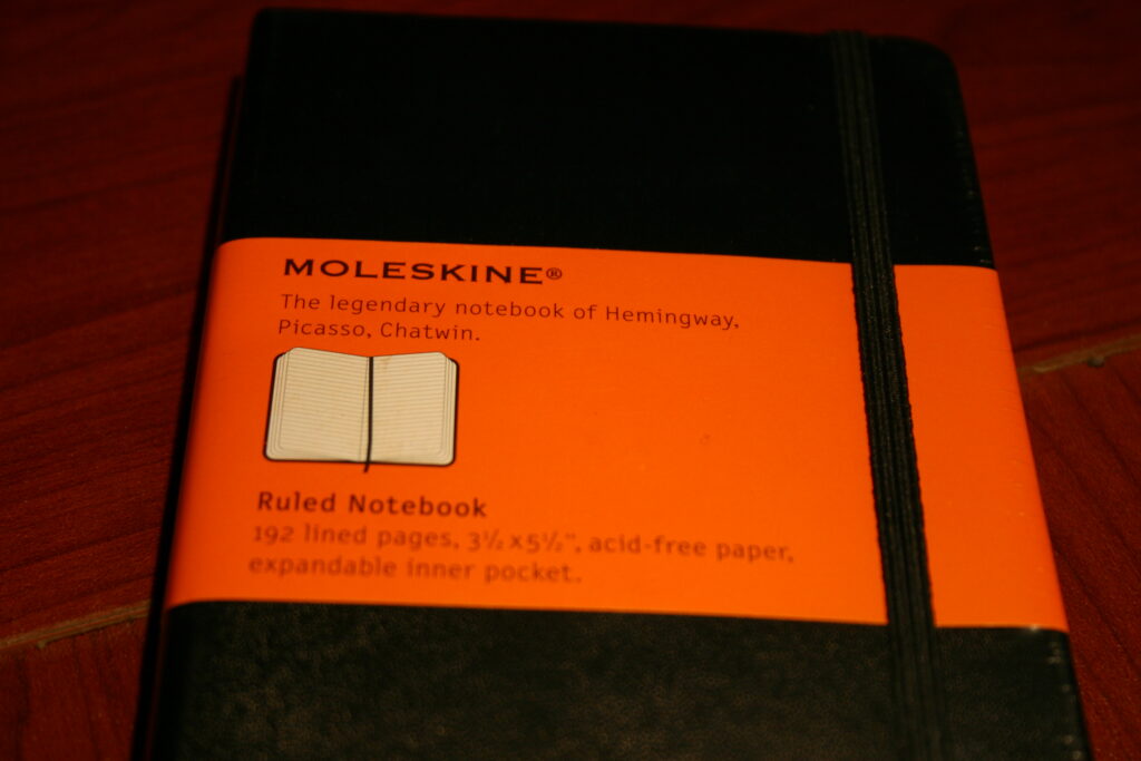 Petit carnet de poche fermé posé sur une table en bois à côté d'un crayon