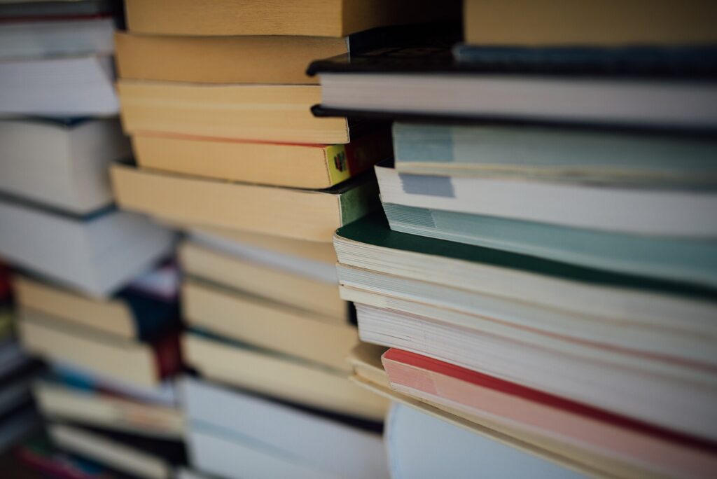 Piles de livres posées à même le sol devant une étagère à moitié vidée